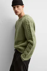 Sweater verde claro de punto con cuello redondo y mangas largas. Presenta diseño de trenzas en el centro y en las mangas.