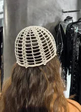 Gorro tipo casquete tejido a crochet color crema, con detalle de perla colgante en el centro.