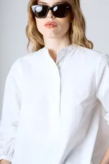 Camisa blanca de corte holgado, cuello mao y mangas largas con puños fruncidos.