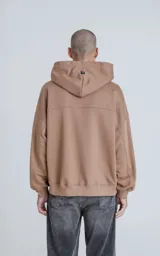 Buzo hoodie marrón de corte oversize, confeccionado en algodón rústico. Tiene capucha forrada, bolsillo tipo bomber con cierre en la manga y bolsillo canguro.