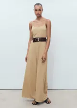 Mono largo color beige, de tirantes finos y corte recto. Incluye cinturón ancho de cuero marrón con hebilla plateada.
