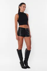 Short negro de cuerina, tiro medio, con bolsillos laterales y traseros, presillas en la cintura y botón metálico.
