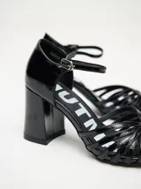 Sandalias negras de charol con tiras cruzadas en el empeine, pulsera con hebilla al tobillo y tacón cuadrado.