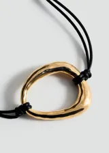 Gargantilla de cordón negro con dije circular dorado y cierre de mosquetón con cadena dorada ajustable.