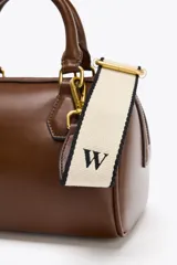 Bolso marrón formato city con asa doble de mano con detalles metálicos y correa interior extraíble en tejido canvas con posición bandolera. Bolsillo interior con cierre mediante cremallera metálica.