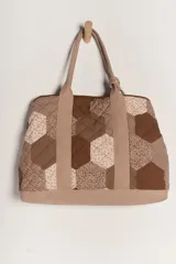 Bolso tipo tote amplio con diseño de patchwork hexagonal acolchado en tonos marrones y beige. Presenta tiras de tela lisa color beige para los hombros y una base lisa del mismo color.