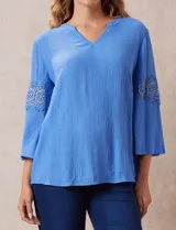 Blusa celeste de gasa bambula con cuello a la base y escote en V. Manga ¾ amplia, con aplique de crochet en los puños.
