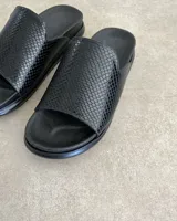 Sandalias chatas color beige con base negra y detalle de bordado blanco en la tira superior.