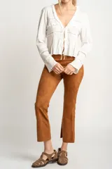Blusa blanca de algodón con escote en V, cierre con lazos, mangas largas con puños elásticos y detalles de encaje y volados.