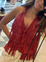 Chaleco de cuero color fucsia, estilo chaleco de flecos, con tachas metálicas plateadas en el frente. Posee un asa de hombro ancha.