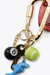 Llavero metálico con mosquetón dorado y charms colgantes desmontables: corazón rojo con espejo interior, llave, pelota de tenis, tiburón azul y bola de billar número 8.