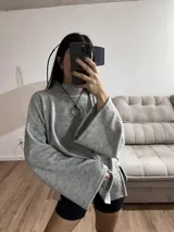 Sweater gris de tejido de punto grueso, con cuello alto, mangas anchas y aberturas laterales.