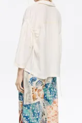 Camisa color crema de corte boxy, confeccionada en mezcla de lino, con cuello camisero, manga 3/4 con sisa ajustable y cierre con botonadura frontal.