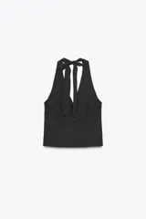 Chaleco negro con estampado de lunares blancos, escote en V, cuello halter con lazo y cierre frontal con botones.