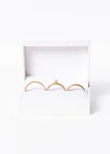 Set de tres anillos dorados, dos alianzas lisas y un cintillo con una piedra engarzada, presentados en un estuche blanco.