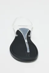 Sandalia plana con tiras de vinilo transparente y suela negra.