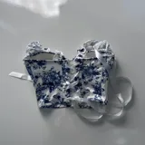 Corset blanco con estampado floral azul, con copas preformadas, tirantes con volantes y lazos ajustables.