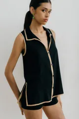 Blusa negra sin mangas con cuello camisero y abertura a los costados, con ribete color beige.