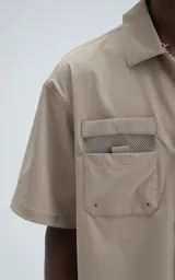 Camisa beige de manga corta, estilo técnica, confeccionada en microfibra liviana. Con doble bolsillo frontal y broches en lugar de botones.