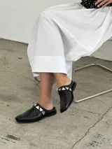 Sueco de cuero negro con detalle de apliques metálicos triangulares plateados.