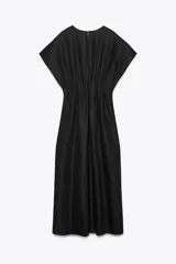 Vestido midi color marrón confeccionado en hilatura con mezcla de algodón y lino. Tiene cuello redondo, manga corta caída y detalle de pliegues en la cintura. Cierre en la espalda con abertura y botón.