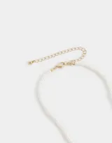 Cadena corta de perlas sintéticas con dije de mariposa dorada y cierre de mosquetón.