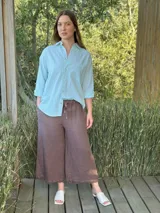 Camisa holgada a rayas verticales color beige y blanco, con cuello clásico, manga larga, bolsillo en el pecho y cierre frontal con botones nacarados.