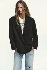 Blazer negro de corte oversize, con cuello solapa, escote pico, manga larga con hombreras y forro interior. Presenta bolsillos con solapa delanteros y bolsillo de vivo en el pecho.