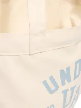 Bolso tote de lona color crema con logo de Under Armour en celeste.