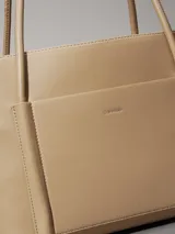 Cartera tote color beige de piel sintética estructurada y suave, con asas tubulares y bolsillo exterior con ranura en la parte delantera. Incluye un bolsillo interior extraíble.