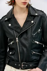 Campera negra de cuero ovino, estilo rocker, con cinturón, charreteras y solapas. Tiene cierres y detalles metálicos en frente y espalda.