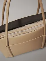 Cartera tote color beige de piel sintética estructurada y suave, con asas tubulares y bolsillo exterior con ranura en la parte delantera. Incluye un bolsillo interior extraíble.