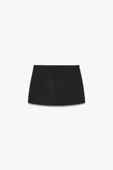 Falda pantalón color crema de tiro bajo con cintura asimétrica, bolsillos delanteros de vivo y cierre lateral con cremallera oculta.