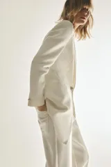 Blazer larga color blanco, de cuello solapa y manga larga con hombreras. Tiene bolsillos delanteros, forro interior y cierre frontal con botón metálico en relieve.