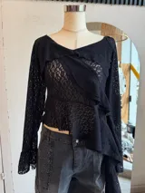 Blusa de encaje color rosa pálido con volados asimétricos y mangas largas acampanadas.