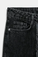 Pantalón de jean de tiro alto con diseño de bloques de color en negro y gris. Cuenta con cinco bolsillos, cierre frontal con cremallera y botón metálico.