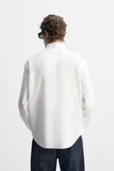 Camisa blanca de corte regular fit confeccionada en popelín de algodón. Tiene cuello abotonado, manga larga con puños abotonados y cierre frontal con botones.