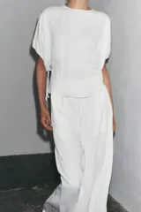 Blusa blanca de lyocell con cuello redondo, manga corta abullonada ajustable con cordones, bajo redondeado y cierre en la espalda con abertura y botón.