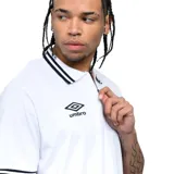 Polo Umbro blanco de manga corta con cuello y puños a rayas negras. Presenta un cierre parcial con cremallera en el escote y el logo Umbro bordado en el pecho.