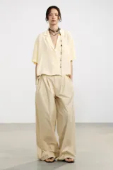 Camisa color amarillo pálido de tejido fluido, con cuello solapa, escote pico, manga corta, bolsillo de parche en el pecho y cierre frontal con botones.