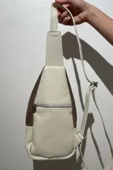 Mochila bandolera de cuero color marrón chocolate y detalles en color crema. Tiene dos bolsillos con cierre y correa regulable.