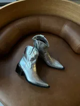 Bota texana de caña corta color plateado, con cierre lateral y bordados decorativos.