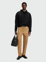 Buzo negro con capucha y cordones ajustables, corte holgado y pequeño logo bordado en el pecho. Se lleva sobre una camisa blanca de cuello.