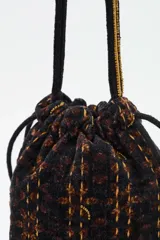 Bolso tipo saco o 'bucket bag' de terciopelo con estampado animal print en tonos marrón oscuro y negro. Presenta costuras verticales en hilo dorado y cordones ajustables negros con borlas y cuentas doradas en los extremos.