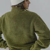Buzo de polar verde oliva con corte a la altura del pecho en tela lisa color verde militar. Cierre frontal con cremallera amarilla y bolsillo tipo canguro con etiqueta de la marca.