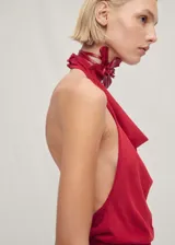 Top rojo de punto fino con cuello halter drapeado y espalda descubierta. Presenta cierre de botones en el cuello, bajo asimétrico y cinturón tipo lazo en la cintura.