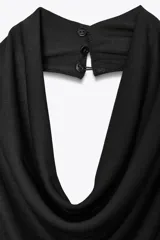 Vestido largo negro con cuello halter y escote fluido, hombros descubiertos, detalle de drapeado en los laterales, forro interior a tono, bajo con abertura en la espalda y cierre lateral con cremallera oculta y botones en el cuello.