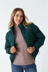 Campera puffer verde oscuro de nylon, con cuello alto, cierre frontal con cremallera, bolsillos laterales y cintura ajustable con cordón.
