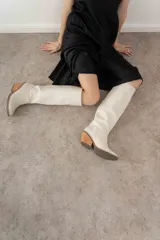 Bota de caña alta color crema, confeccionada en cuero texturizado, con punta cuadrada y taco de madera.