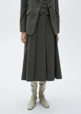 Falda midi gris jaspeado de tejido mezcla de lana, con tiro medio, diseño evasé y tablas. Cierre de cremallera invisible en la parte posterior.